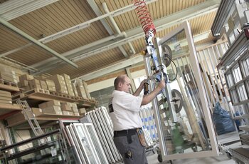 Kransystem mit Vakuumheber für Fenstertransport Ein fertig montiertes Fenster wird mittels Kran vom Arbeitstisch angehoben und zum Transportwagen gebracht