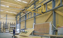 In a carpentry workshop, wooden boards are transported by means of a crane system